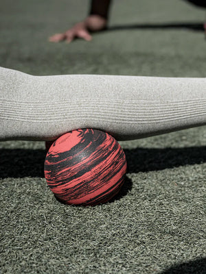 Person holding a red and black striped ball on a grassy surface. Roller-Peanut-Foam-COREFX Red and black marbled object on a white background